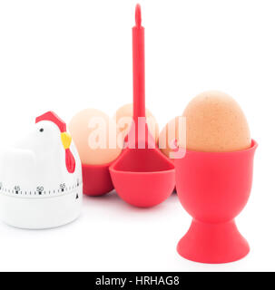 Boiled chicken eggs in a red egg cup and red holder with egg timer isolated on white. Stock Photo