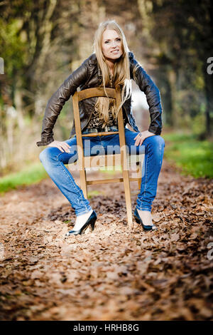 Model released, Blonde, attraktive Frau posiert auf einem Stuhl im Herbst - young, attractive woman posing on a chair in autumn Stock Photo