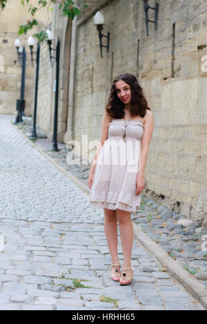 Full length portrait of curlie young girl wearing biege romantic dress strolling through old streets of Inner City of Baku Stock Photo