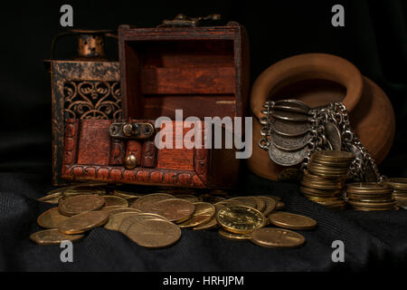 Treasure chest, pile and pillar of coins, a ceramic bowl filled with jewelry coins and candle lamp in dark environment Stock Photo