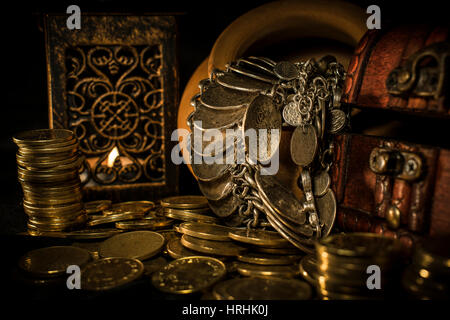 Treasure chest, pile and pillar of coins, a ceramic bowl filled with jewelry coins and candle lamp in dark environment Stock Photo