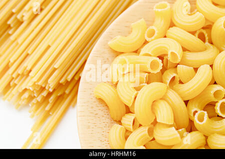 Raw elbow macaroni in wooden dish with raw pasta on white background. Stock Photo