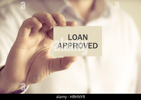 Closeup on businessman holding a card with text LOAN APPROVED, business concept image with soft focus background and vintage tone Stock Photo