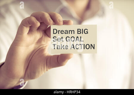 Closeup on businessman holding a card with text DREAM BIG, SET GOAL, TAKE ACTION, business concept image with soft focus background and vintage tone Stock Photo