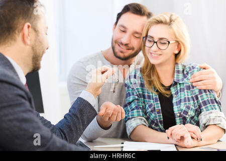 Dealership concept. Bank concept. Toned of sales manager ready to give key to young couple in love after signing agreement or contract for purchase or Stock Photo