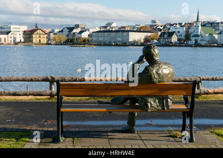 Sculpture of a man sitting on a park bench in front of Tjornin Lake and the Historic Centre of Rykjavik, Iceland, Polar Regions Stock Photo