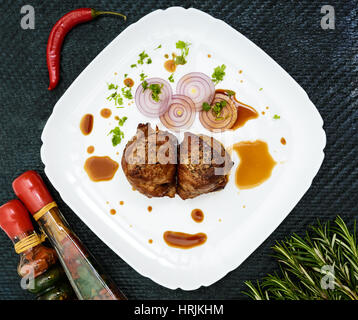Juicy pork medallions wrapped in bacon on a plate on the dark background. The top view