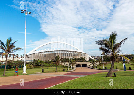 DURBAN, SOUTH AFRICA - FEBRUARY 24, 2017:  Unknown early morning jogger, paved promenade, green grass lawn and palm trees against Moses Mabhida Stadiu Stock Photo