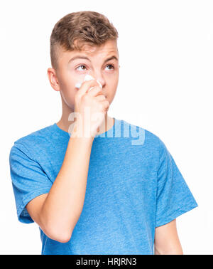 Healthcare and medicine concept - ill teen boy with flu blowing nose. Teenager wipes a nose a napkin. Child wearing blue t-shirt, isolated on white ba Stock Photo