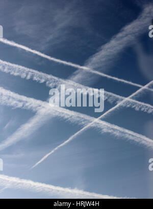 Multiple contrails crossing against blue sky and cirrus cloud and drifting in the wind Stock Photo