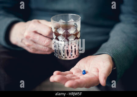 A senior man golding glass of hot tea and blue pill in other hand. Senility concept Stock Photo