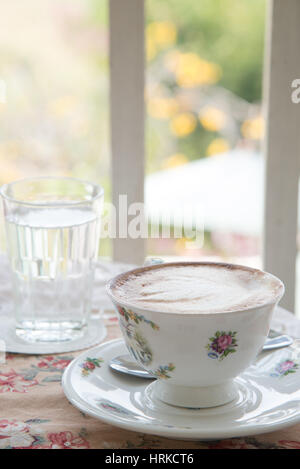 Cafe art latte coffee in the vintage cup on the tabel with a glass of water on the table Stock Photo