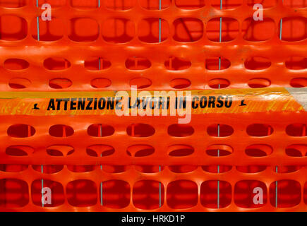 Plastic orange safety net to delimit the area of a road construction site with ITALIAN words meaning CAUTION WORK IN PROGRESS Stock Photo