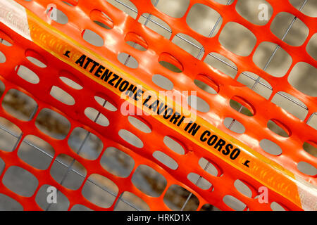 Plastic orange safety net to delimit the area of a road construction site with ITALIAN words meaning CAUTION WORK IN PROGRESS Stock Photo