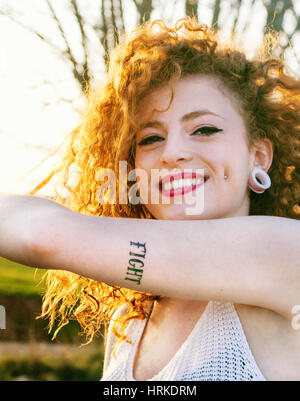 Young alternative redhead woman with piercings and tattooes enjoying the sunset at summer Stock Photo