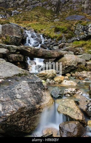 A small mountain stream and primitive stone bridge on the Cwm Idwal track in the Snowdonia National Park in North Wales. Shot with a long exposure to  Stock Photo