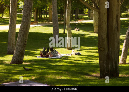 A couple and a person in the background enjoying the summer afternoon sun in El Retiro Park, Madrid, Spain Stock Photo