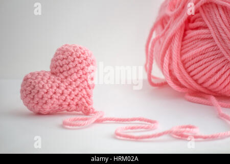 Adorable little heart crocheted by hand. Made with a thread of a thick bulky wool thread. The thread is not cut and still attached to the heart. Stock Photo