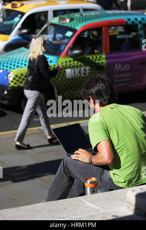 A male sits on steps in a London Street working on his laptop. Stock Photo