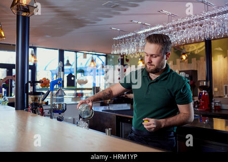 The bartender with beard behind bar pours a drink into  glass Stock Photo