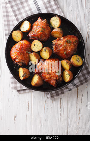 Roast chicken thighs and baby potatoes with maple syrup closeup on a plate. vertical view from above Stock Photo