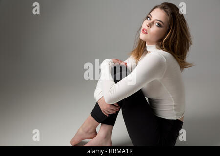 Studio portrait of a beautiful young woman sitting on floor Stock Photo