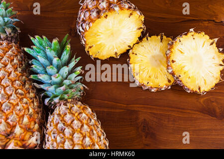 Two whole and some cutting slices pineapples on wooden table, top view Stock Photo