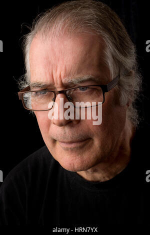 close up portrait head shot of a senior man in his 50's. male wearing black t-shirt and isolated on black background. Stock Photo