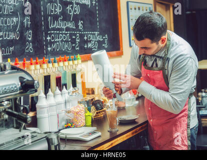 Barista pours gentle cream into the cup for the cappuccino in the cozy cafe. Stock Photo