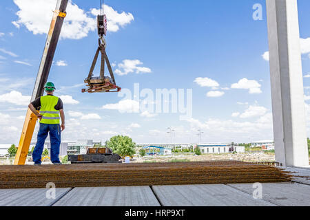 Crane hook with straps is raising palette on the unfinished hall. Stock Photo