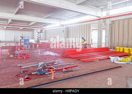 Workers are painting long round pipes in red using an airbrush gun at construction site. Stock Photo