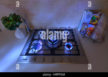 Close up view of burners alight on a five burner hob with blue ambient lighting. Stock Photo