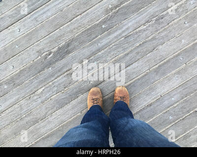 Point of view (POV) looking down at feet, standing on a wooden boardwalk at Coney Island, Brooklyn, New York.  Looking down at brown shoes wearing den Stock Photo