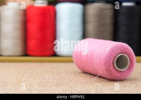 Pink spools of thread on sackcloth table Stock Photo