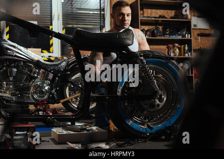 Like shade. Serious bearded man having relief body being keen on motorbikes posing behind his iron friend Stock Photo