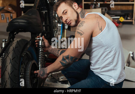 Keep it. Brutal young man wearing jeans and white vest putting his hands on the wheel while keeping his head turned to camera Stock Photo