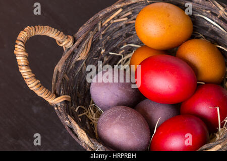 Wicker basket with colorful Easter eggs on wooden table, closeup Stock Photo