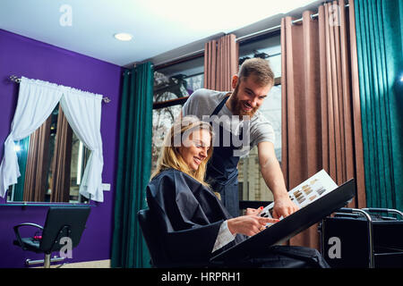 Woman client chooses the color of paint with hair stylist man in a beauty salon. Stock Photo