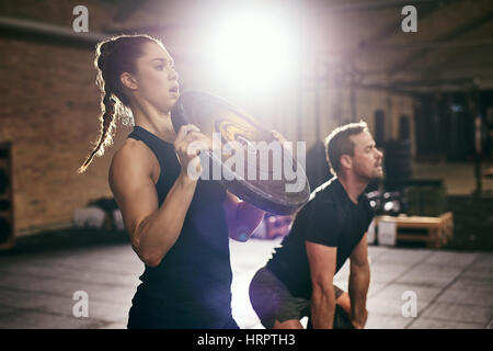 Sportive man and woman having workout with heavy round weight disks in spacious gym. Stock Photo