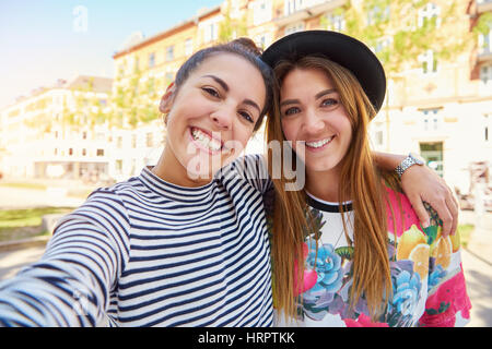Pair of cute girlfriends in striped and flowery shirts embracing outside as if to pose for a photograph Stock Photo
