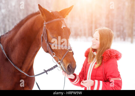 Teenage girl feeding bay horse on winter field. Friendship concept image Stock Photo