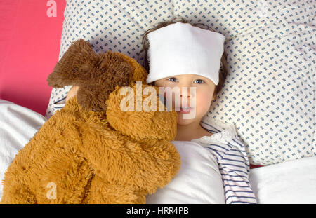 little girl with a headache in bed with teddy bear Stock Photo