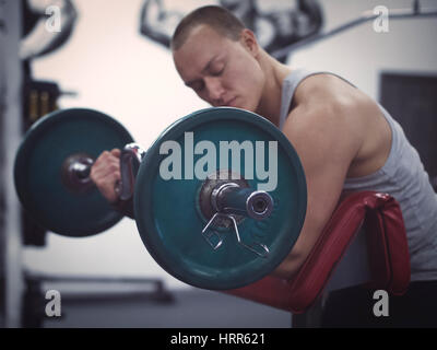 side view of muscular man holding barbell in gym. Focus on barbell. Training in gym concept. Toned image. Low key. Shallow DOF Stock Photo