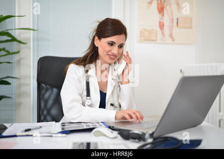 Doctor talking on the phone while using a laptop in her studio Stock Photo