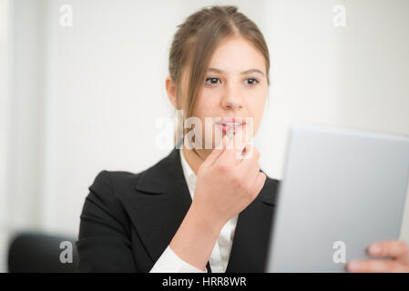 Woman using her tablet as a mirror to put on some lipstick in the office Stock Photo