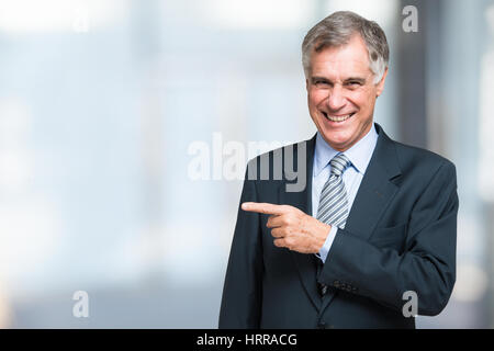 Smiling senior businessman pointing his finger on the white space Stock Photo