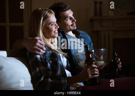 side view of smiling couple watching movie with popcorn and beer Stock Photo