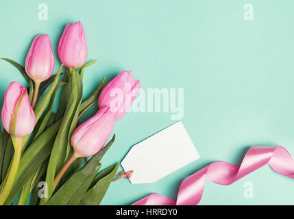 Pink tulips, ribbon and empty gift tag on pastel green background. Spring concept. Stock Photo