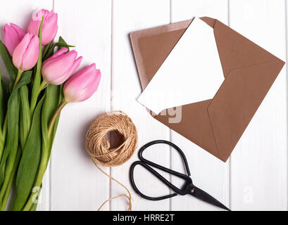 Pink tulips, envelope, scissors and jute rope on the white table, top view Stock Photo