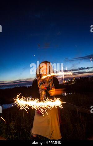 A woman holding sparklers at dusk celebrating the 4th of July at Birch Bay, Washington, USA. Stock Photo